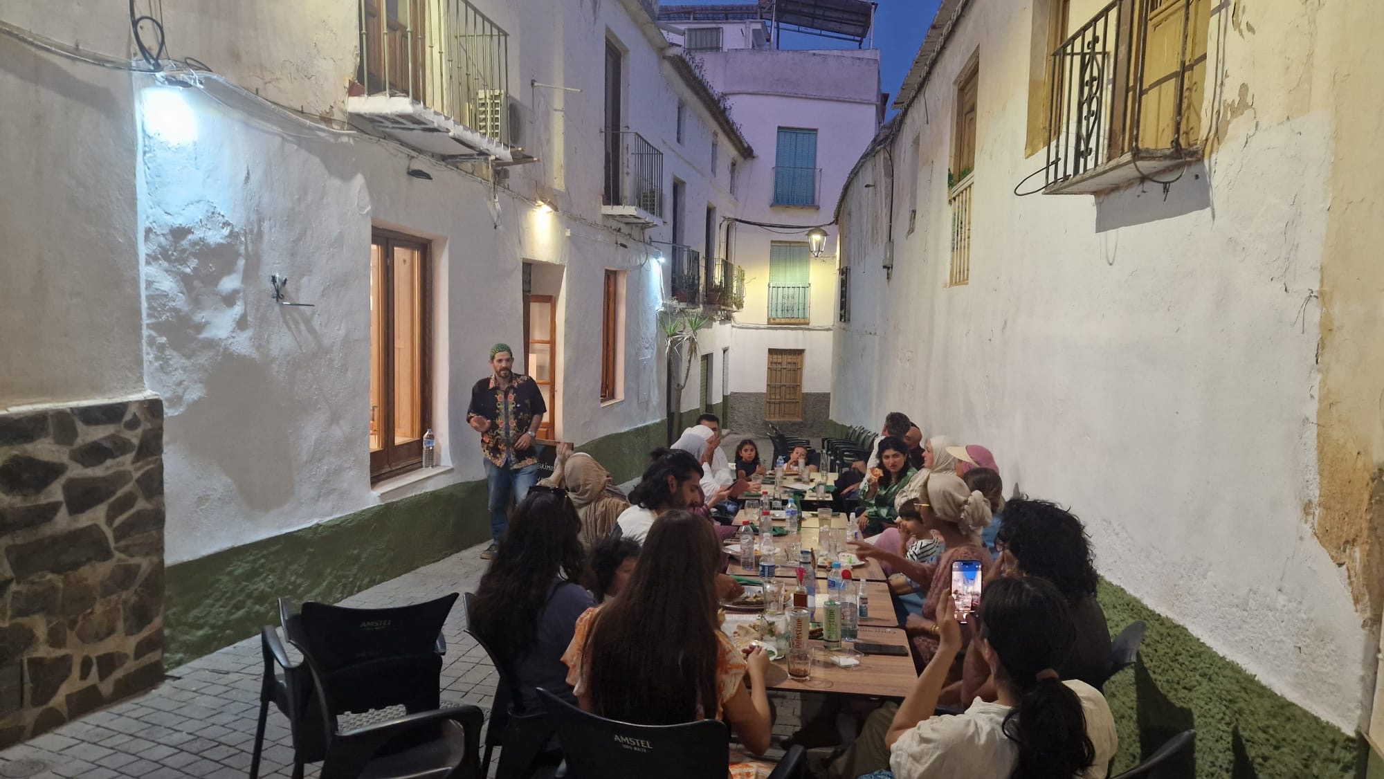 Guests sharing a long communal table on a whitewashed Órgiva street at dusk